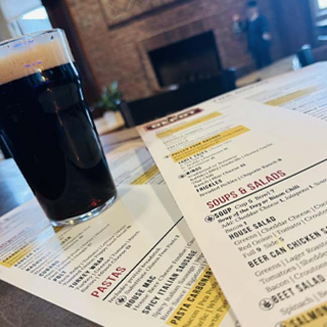 A glass of dark beer sits on a bar table with Green Bay restaurant menus in the foreground.