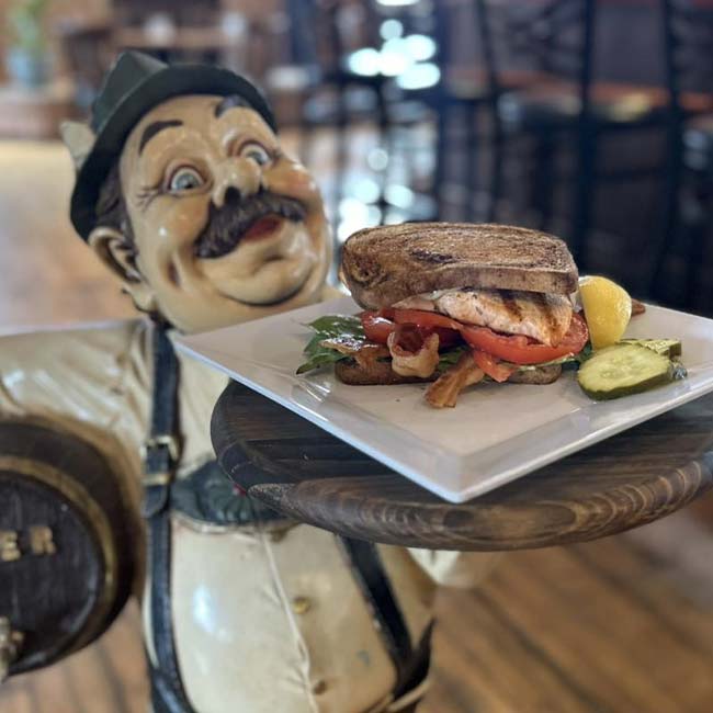 A statue waiter at The Depot holds a sandwich, pickle, lemon, and drink in Green Bay.