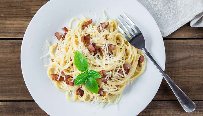 Plate of spaghetti with bacon, grated cheese, and basil—perfect for a Family Restaurant meal.