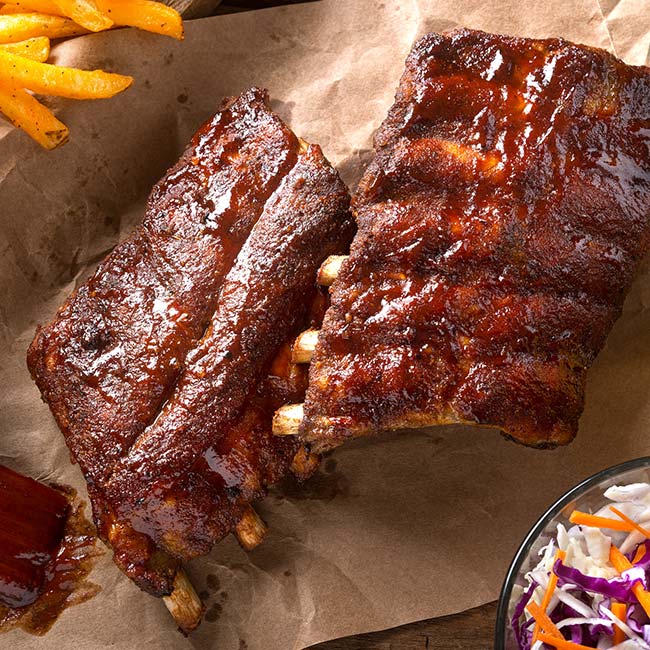 Barbecue ribs on brown paper with fries and coleslaw at a cozy family restaurant.
